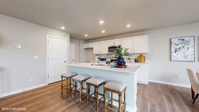 kitchen with a breakfast bar, a kitchen island with sink, light hardwood / wood-style flooring, appliances with stainless steel finishes, and white cabinetry