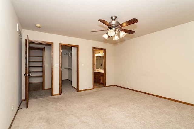 unfurnished bedroom with ensuite bathroom, a spacious closet, light colored carpet, ceiling fan, and a closet