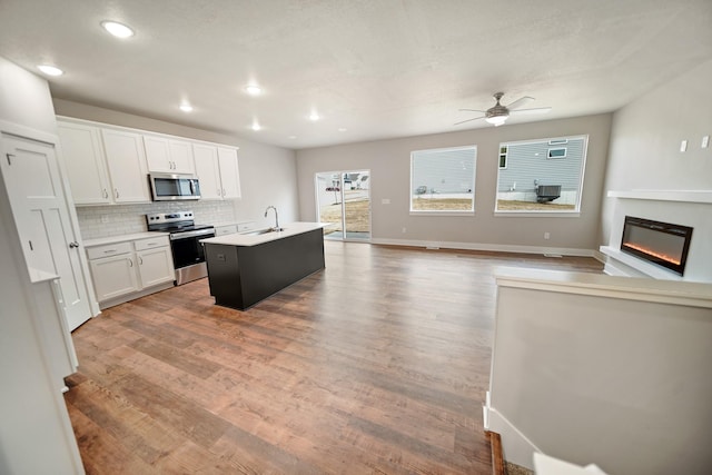 kitchen featuring sink, white cabinetry, backsplash, stainless steel appliances, and an island with sink