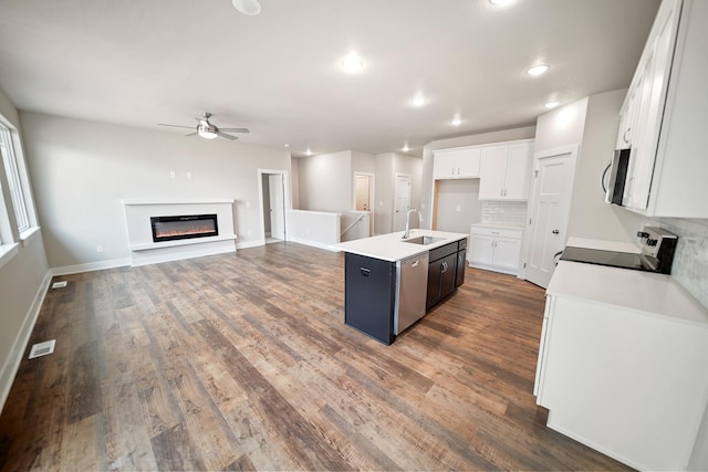 kitchen with sink, a kitchen island with sink, white cabinetry, stainless steel appliances, and decorative backsplash