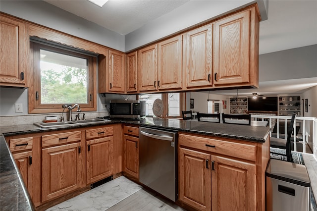 kitchen featuring sink, kitchen peninsula, appliances with stainless steel finishes, dark stone countertops, and light wood-type flooring