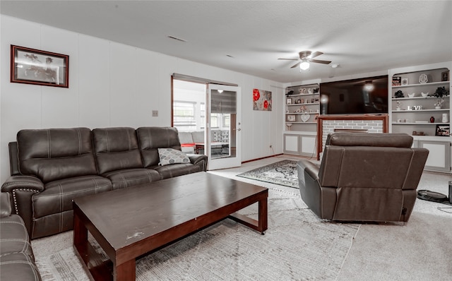 living room with a textured ceiling, built in shelves, light colored carpet, a brick fireplace, and ceiling fan