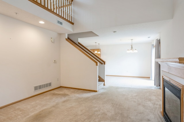 unfurnished living room with a high ceiling, light carpet, a high end fireplace, and a notable chandelier