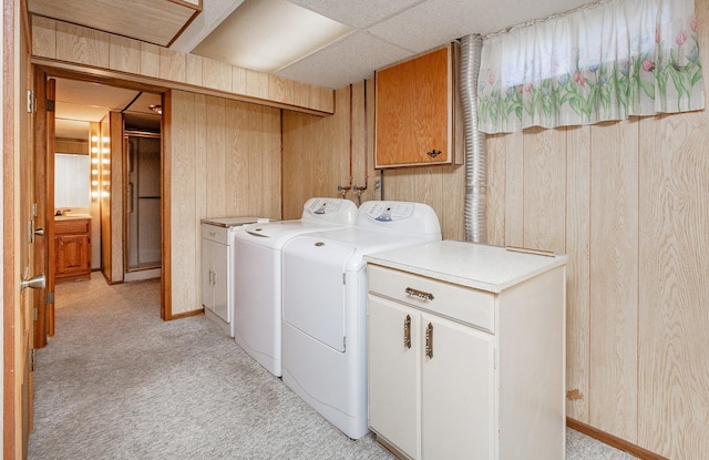 clothes washing area with cabinets, wood walls, light colored carpet, and washing machine and clothes dryer