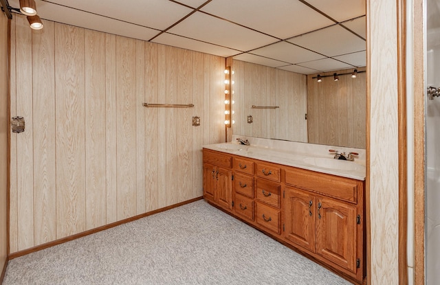 bathroom with a paneled ceiling, vanity, and wood walls