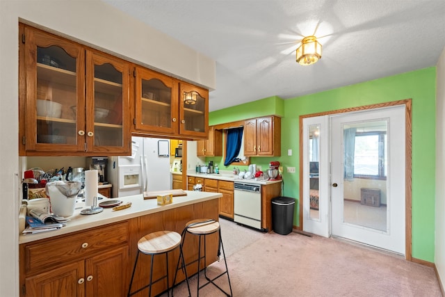 kitchen featuring white appliances, kitchen peninsula, a textured ceiling, a kitchen bar, and light colored carpet