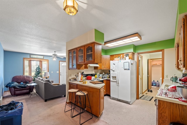 kitchen featuring light colored carpet, a textured ceiling, a kitchen breakfast bar, and white appliances