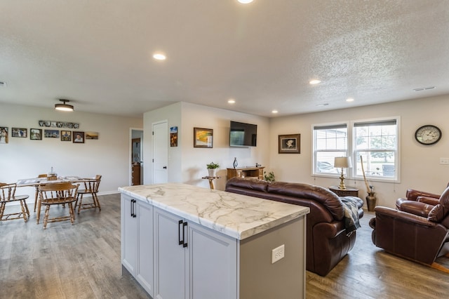 kitchen featuring light wood-type flooring, a textured ceiling, a kitchen island, and light stone counters