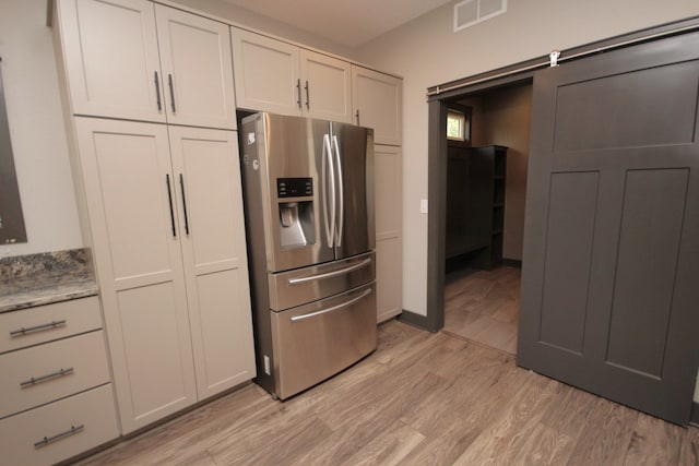 kitchen with white cabinets, light stone countertops, stainless steel refrigerator with ice dispenser, light wood-type flooring, and a barn door