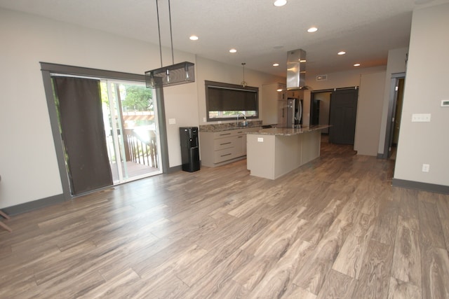 kitchen with light stone counters, light wood-type flooring, stainless steel fridge, and a kitchen island