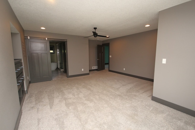 carpeted spare room with ceiling fan, a textured ceiling, and a barn door