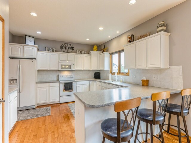 kitchen with light wood-type flooring, kitchen peninsula, white appliances, and white cabinetry