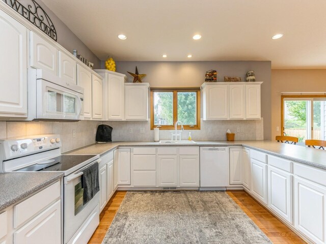 kitchen with sink, white appliances, white cabinetry, light wood-type flooring, and decorative backsplash