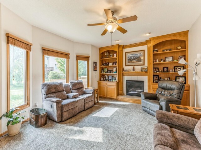 carpeted living room featuring a tile fireplace, built in shelves, and ceiling fan