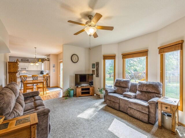 carpeted living room with ceiling fan with notable chandelier