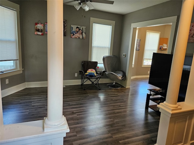 living area with ceiling fan, decorative columns, and dark hardwood / wood-style flooring