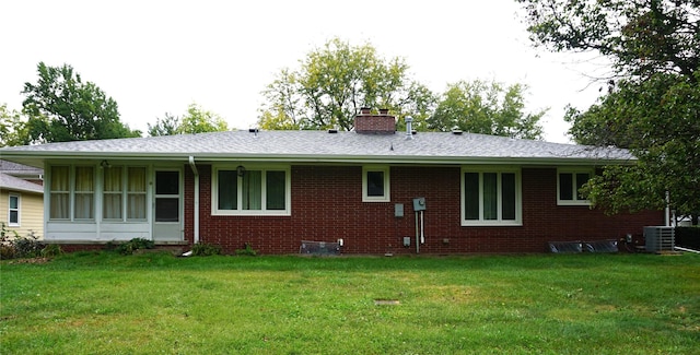 back of property featuring brick siding, a shingled roof, central AC unit, a lawn, and a chimney