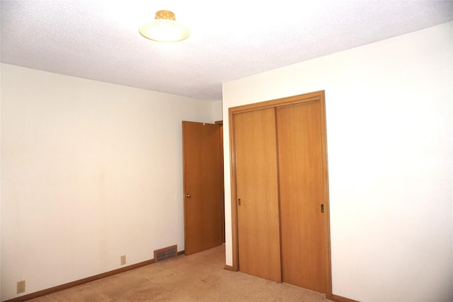 unfurnished bedroom featuring visible vents, a textured ceiling, a closet, baseboards, and light colored carpet