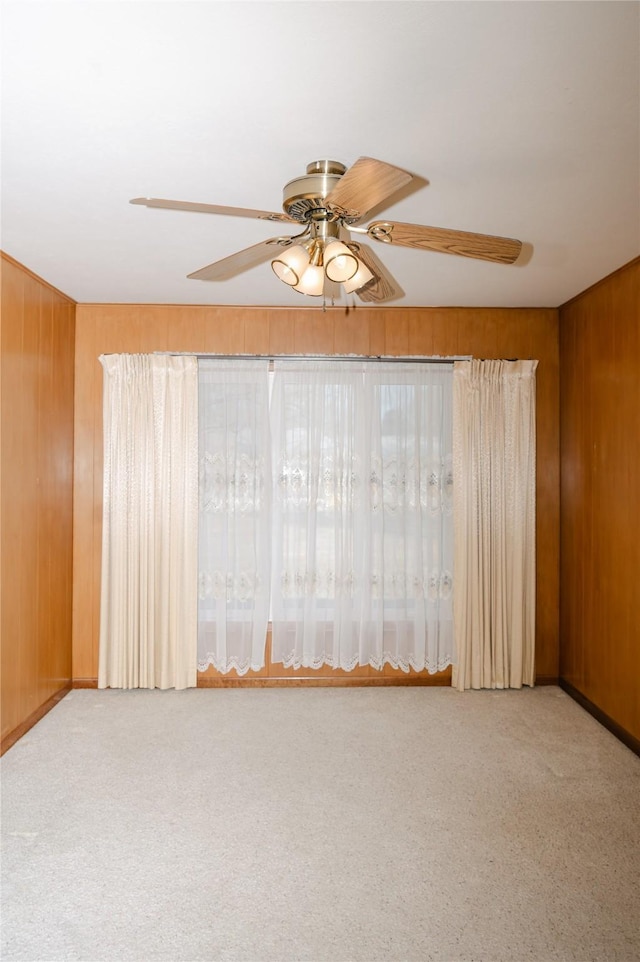 carpeted empty room featuring wood walls and a ceiling fan