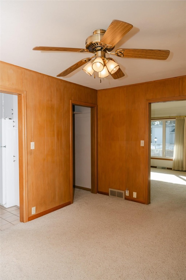 empty room with a ceiling fan, visible vents, wood walls, and light carpet