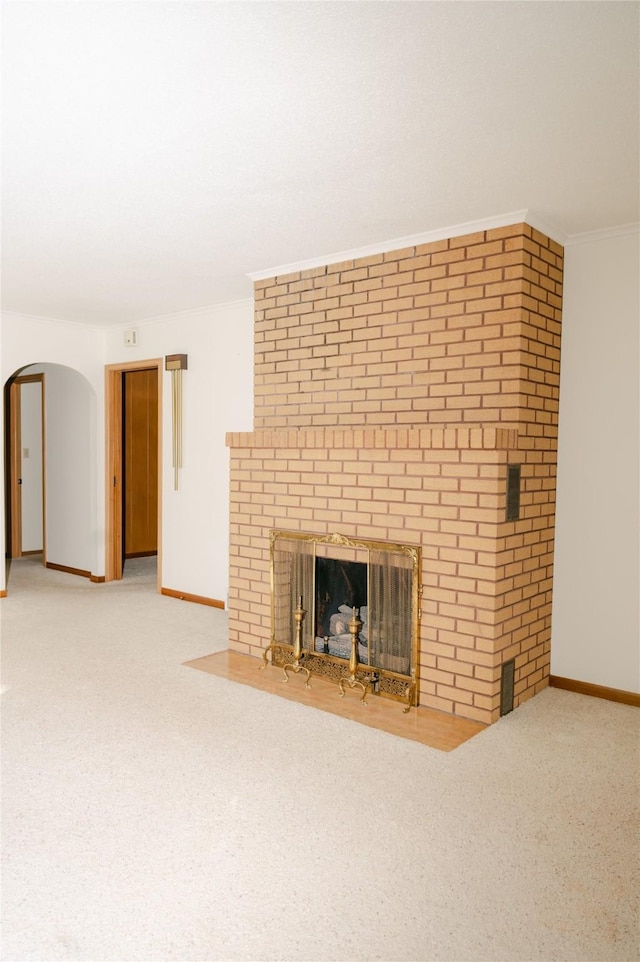 unfurnished living room with arched walkways, carpet flooring, a brick fireplace, and ornamental molding