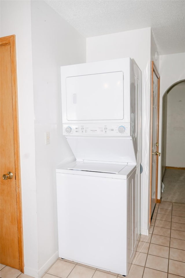 laundry area with a textured ceiling, stacked washing maching and dryer, arched walkways, light tile patterned floors, and laundry area