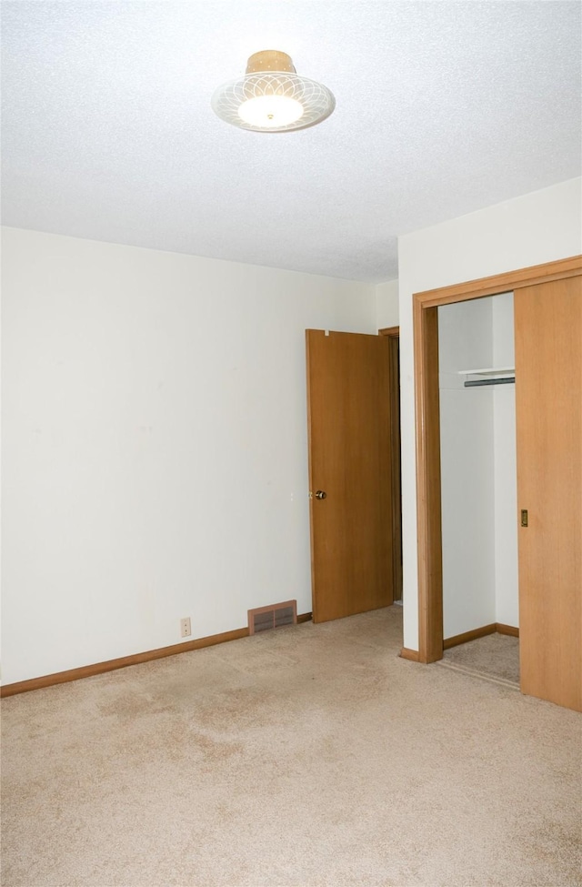 unfurnished bedroom with visible vents, light colored carpet, a closet, and a textured ceiling