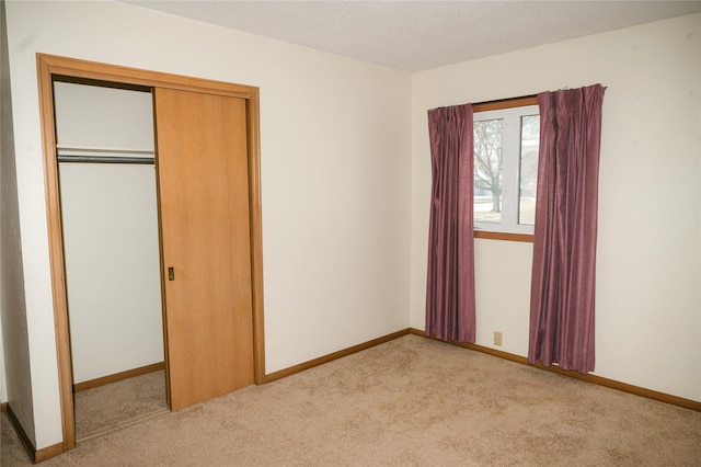 unfurnished bedroom with light colored carpet, a closet, and baseboards