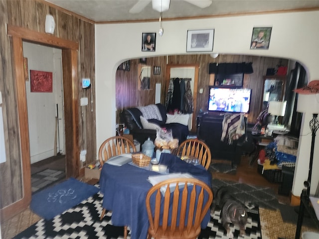 dining room with ornamental molding, wood walls, and ceiling fan