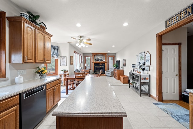 kitchen featuring a large fireplace, black dishwasher, ceiling fan, and a kitchen island