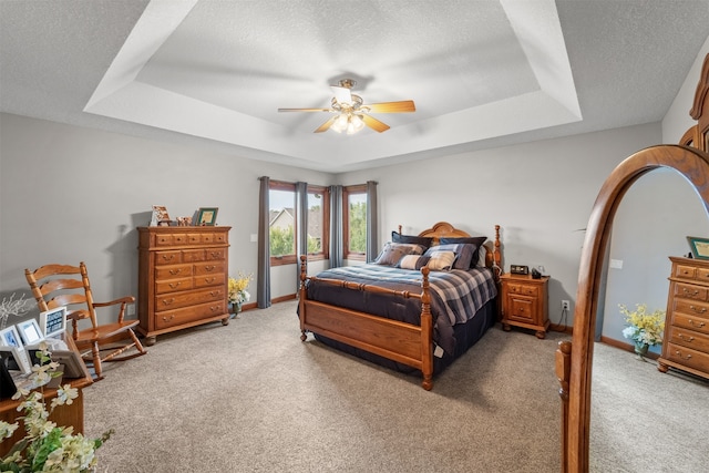 carpeted bedroom with ceiling fan, a raised ceiling, and a textured ceiling