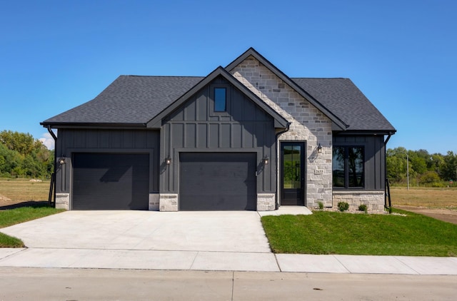 view of front of home featuring a garage, board and batten siding, a front yard, and stone siding