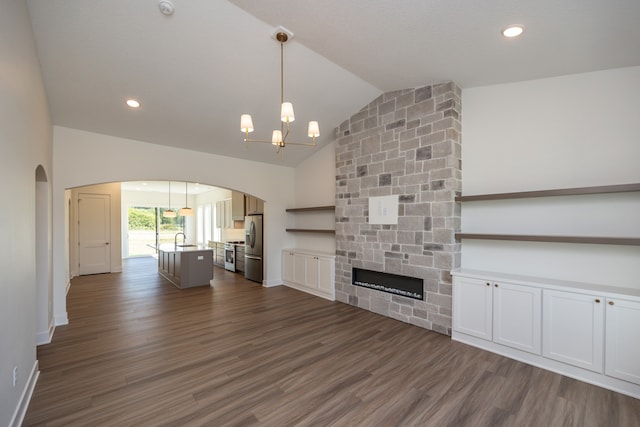 unfurnished living room with dark wood-type flooring, a stone fireplace, sink, an inviting chandelier, and high vaulted ceiling