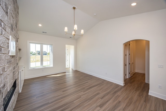 unfurnished living room with dark hardwood / wood-style floors, lofted ceiling, a stone fireplace, and a chandelier