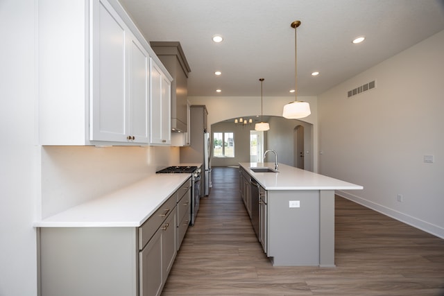 kitchen featuring sink, decorative light fixtures, dark hardwood / wood-style flooring, stainless steel appliances, and a kitchen island with sink