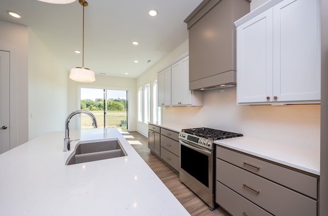 kitchen with sink, stainless steel gas stove, white cabinetry, light stone counters, and decorative light fixtures