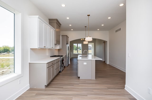 kitchen with a breakfast bar area, gray cabinets, hanging light fixtures, stainless steel appliances, and an island with sink