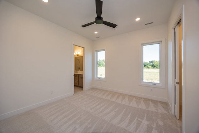 unfurnished bedroom with light carpet, ensuite bath, multiple windows, and ceiling fan