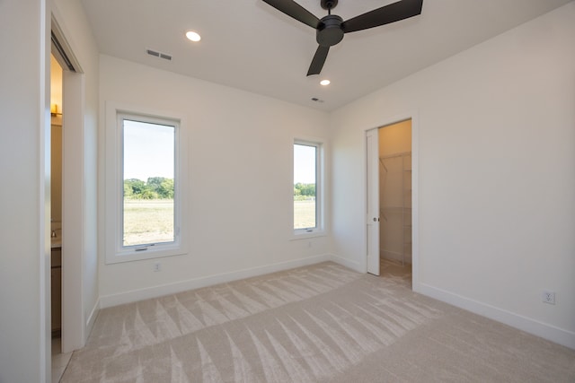 unfurnished bedroom with light carpet, a spacious closet, multiple windows, and a closet