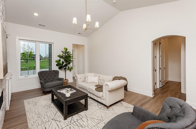living area featuring visible vents, arched walkways, vaulted ceiling, a notable chandelier, and light wood-style floors