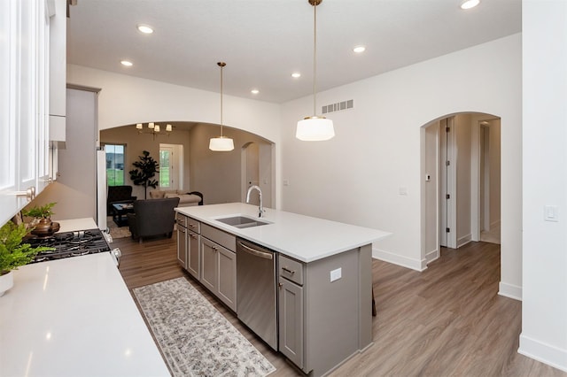 kitchen with a sink, arched walkways, gray cabinets, stainless steel dishwasher, and visible vents