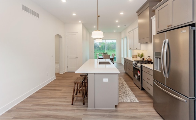 kitchen with appliances with stainless steel finishes, a sink, a kitchen island with sink, light wood-style flooring, and visible vents