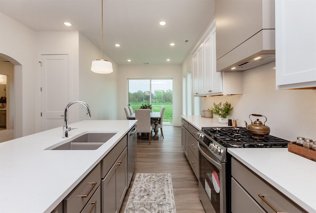 kitchen featuring arched walkways, a sink, light countertops, light wood-style floors, and stainless steel appliances