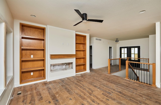 unfurnished living room featuring french doors, visible vents, a textured ceiling, and wood finished floors