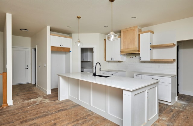 kitchen featuring an island with sink, backsplash, wood finished floors, pendant lighting, and a sink