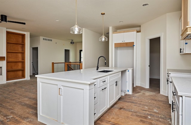 kitchen with a kitchen island with sink, a sink, white cabinetry, dark wood finished floors, and decorative light fixtures