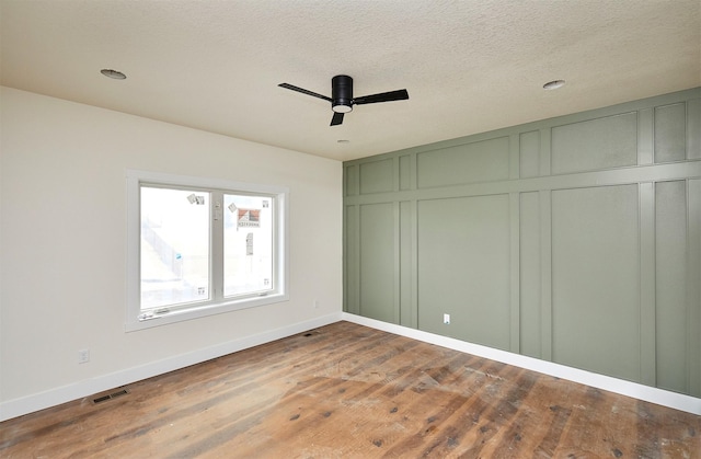 unfurnished bedroom with a closet, visible vents, a decorative wall, a textured ceiling, and wood finished floors