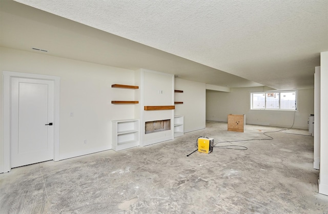 unfurnished living room with built in features, visible vents, a fireplace, and a textured ceiling