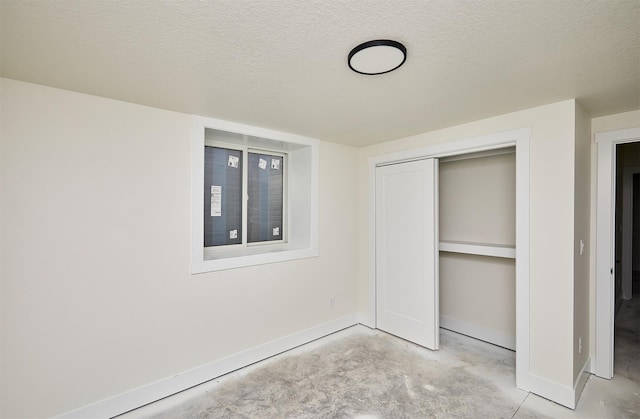 unfurnished bedroom with a textured ceiling, concrete floors, and baseboards