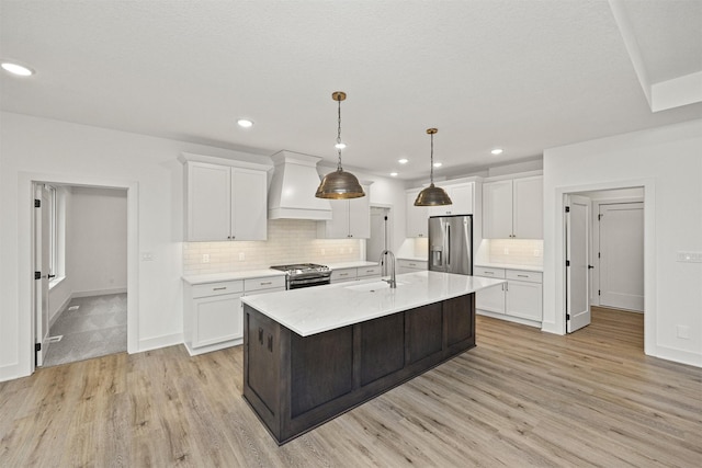 kitchen featuring white cabinets, an island with sink, stainless steel appliances, and custom exhaust hood